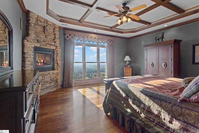 bedroom featuring ornamental molding, coffered ceiling, ceiling fan, wood-type flooring, and a stone fireplace