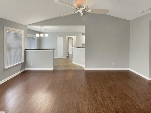 unfurnished living room with ceiling fan with notable chandelier, dark wood-type flooring, and lofted ceiling