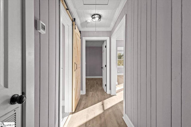 hallway featuring light wood-type flooring, a barn door, and ornamental molding