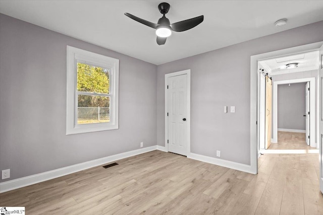 unfurnished bedroom with ceiling fan, a barn door, and light hardwood / wood-style floors