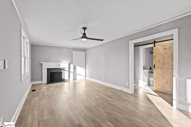 unfurnished living room featuring a barn door, ceiling fan, light hardwood / wood-style flooring, and ornamental molding