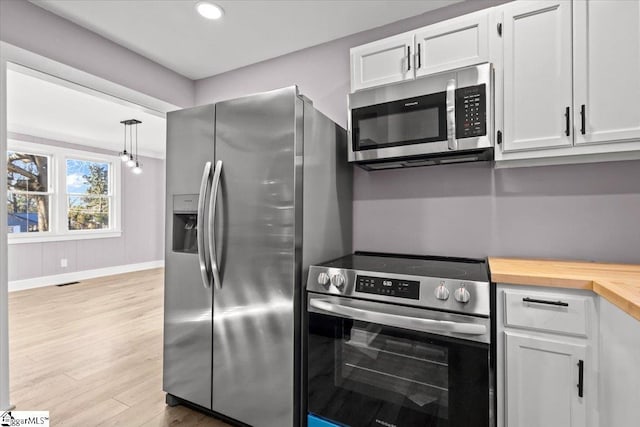 kitchen with pendant lighting, white cabinets, light wood-type flooring, appliances with stainless steel finishes, and butcher block countertops