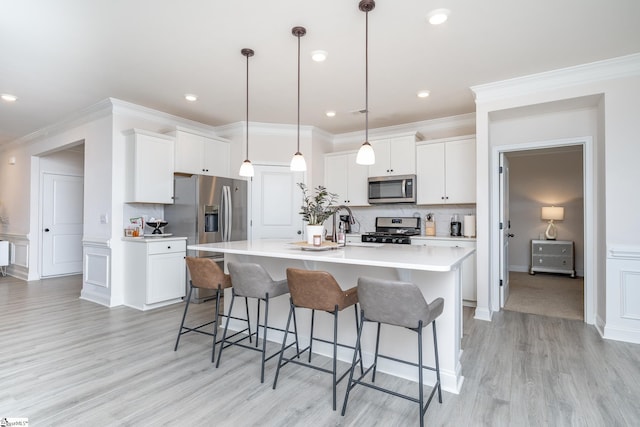 kitchen with white cabinets, decorative light fixtures, stainless steel appliances, and a kitchen island with sink