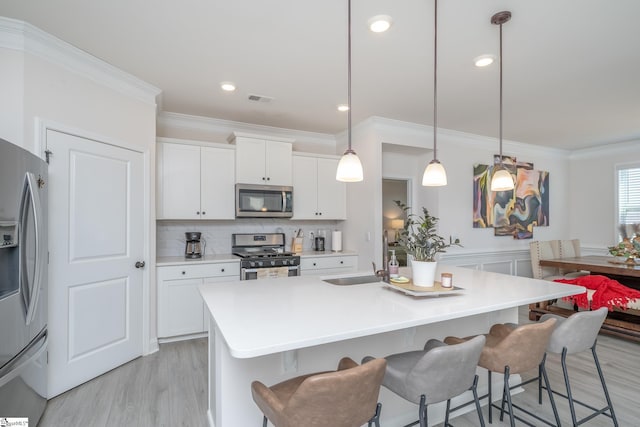 kitchen featuring a kitchen bar, white cabinetry, hanging light fixtures, and appliances with stainless steel finishes