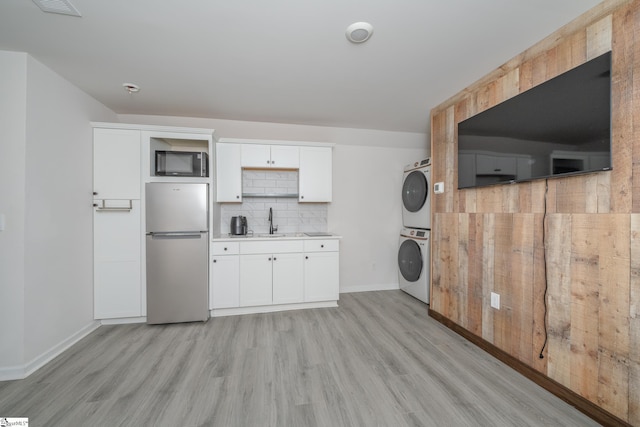 clothes washing area with stacked washing maching and dryer, light hardwood / wood-style flooring, and sink