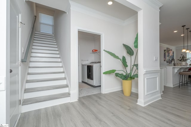 stairs featuring washing machine and dryer, crown molding, sink, and wood-type flooring