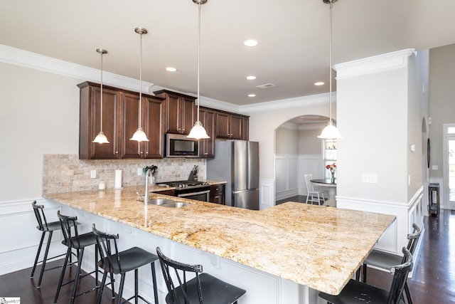 kitchen featuring kitchen peninsula, appliances with stainless steel finishes, a breakfast bar, crown molding, and pendant lighting