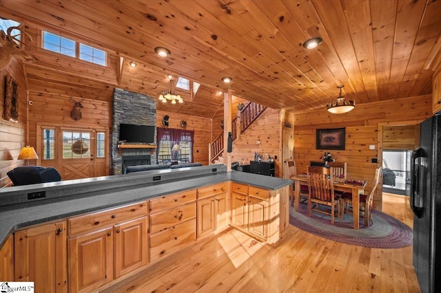 kitchen with black refrigerator, light hardwood / wood-style flooring, wooden ceiling, a stone fireplace, and wood walls