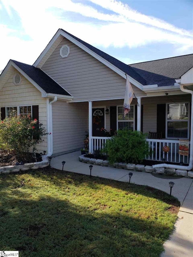 ranch-style home featuring covered porch and a front lawn