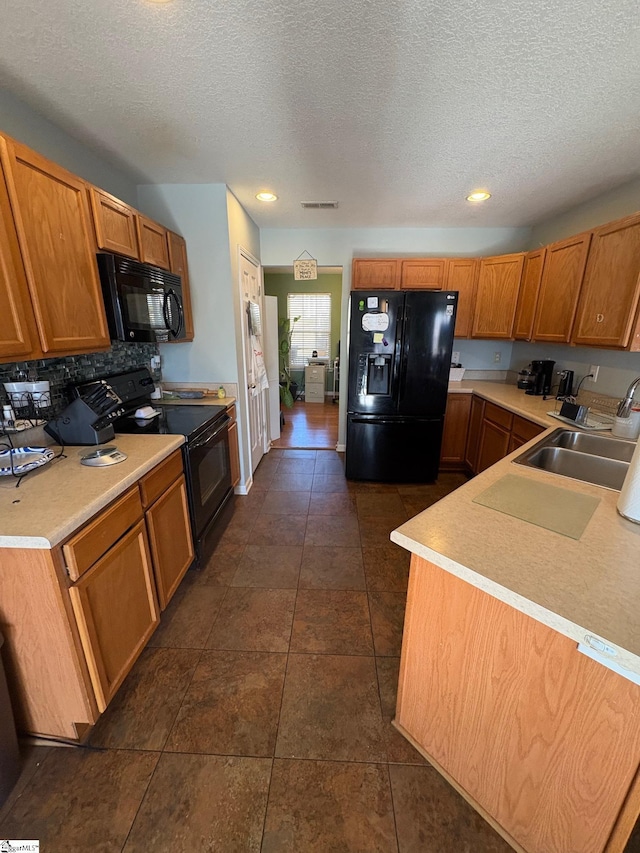 kitchen with sink, a textured ceiling, decorative backsplash, black appliances, and dark tile patterned flooring