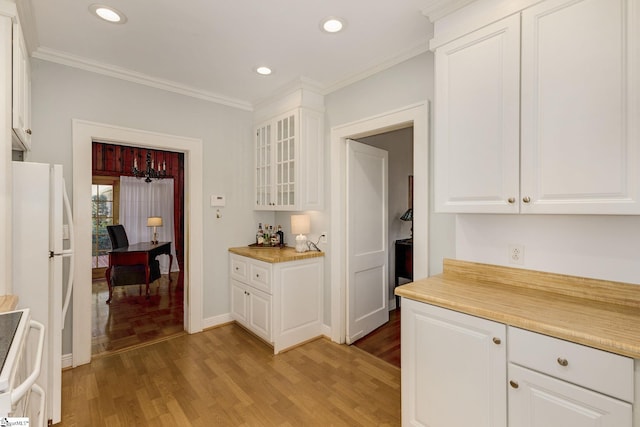 kitchen featuring stove, hardwood / wood-style flooring, ornamental molding, white fridge, and white cabinetry