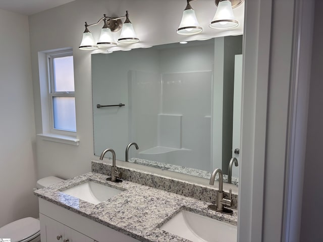 bathroom with double vanity, a sink, and toilet