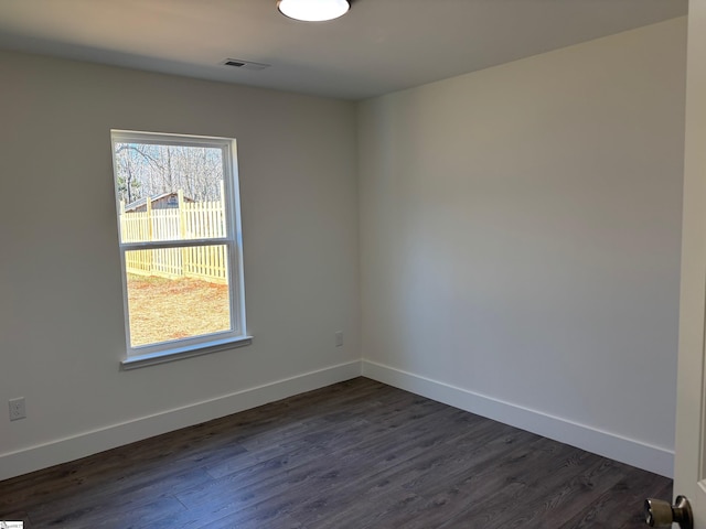 empty room featuring dark wood-style flooring, visible vents, and baseboards