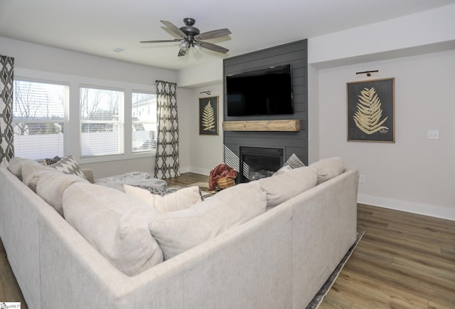 living room featuring ceiling fan, a large fireplace, and dark wood-type flooring