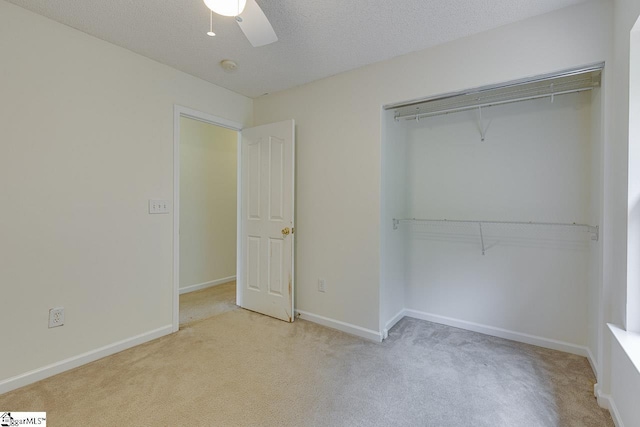 unfurnished bedroom with a textured ceiling, light colored carpet, a closet, and ceiling fan