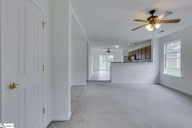 unfurnished living room with light carpet, a textured ceiling, and ceiling fan