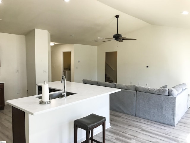 kitchen featuring vaulted ceiling, ceiling fan, a center island with sink, light hardwood / wood-style flooring, and a breakfast bar area