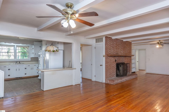 kitchen with white cabinets, sink, a brick fireplace, beam ceiling, and white fridge