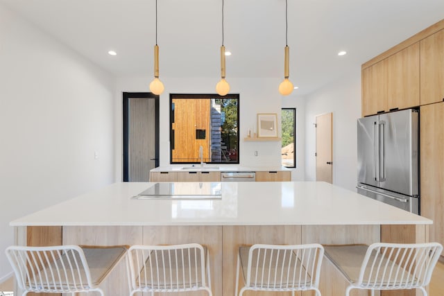 kitchen featuring a kitchen island, light brown cabinetry, hanging light fixtures, and appliances with stainless steel finishes