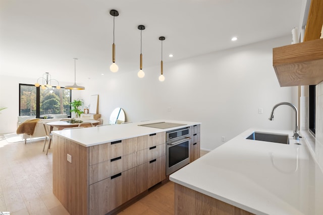 kitchen with light wood-type flooring, stainless steel oven, a spacious island, sink, and hanging light fixtures