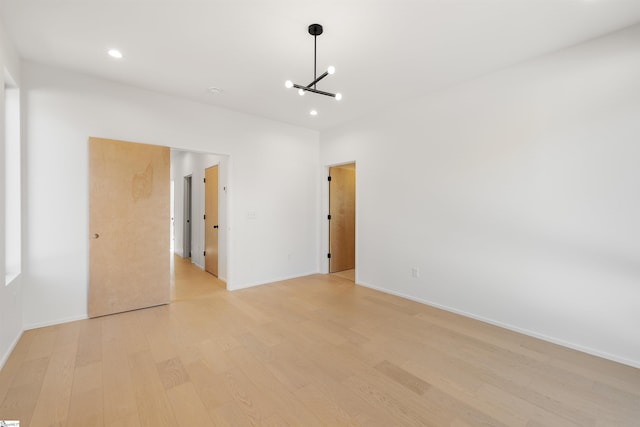 spare room featuring light wood-type flooring and a notable chandelier