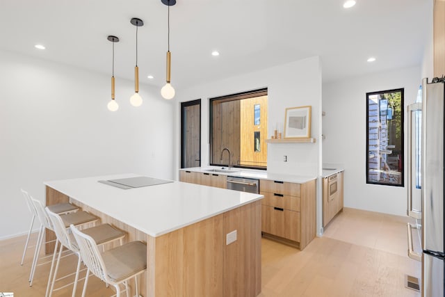 kitchen featuring light wood-type flooring, stainless steel appliances, sink, decorative light fixtures, and a kitchen island