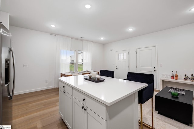 kitchen with a kitchen island, white cabinetry, stainless steel fridge, a kitchen breakfast bar, and light hardwood / wood-style flooring