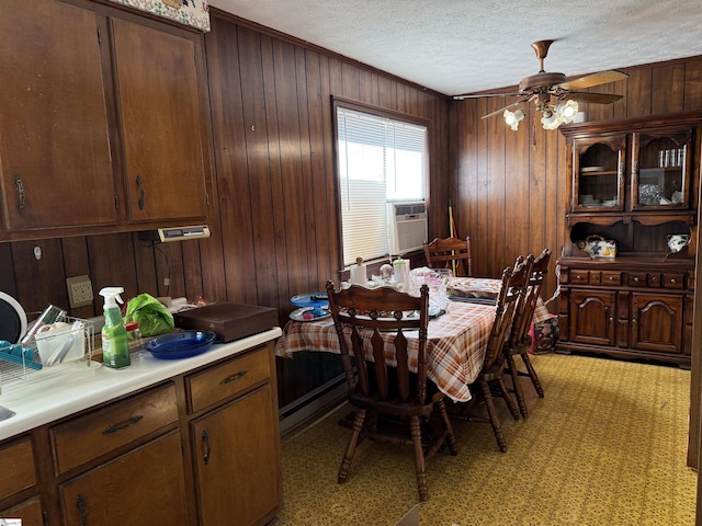 dining space with ceiling fan, baseboard heating, light colored carpet, a textured ceiling, and wooden walls