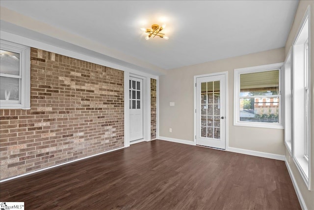 spare room featuring dark hardwood / wood-style floors, a healthy amount of sunlight, and brick wall