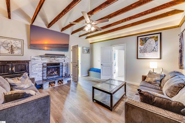 living room with light wood-type flooring, lofted ceiling with beams, a stone fireplace, and ceiling fan