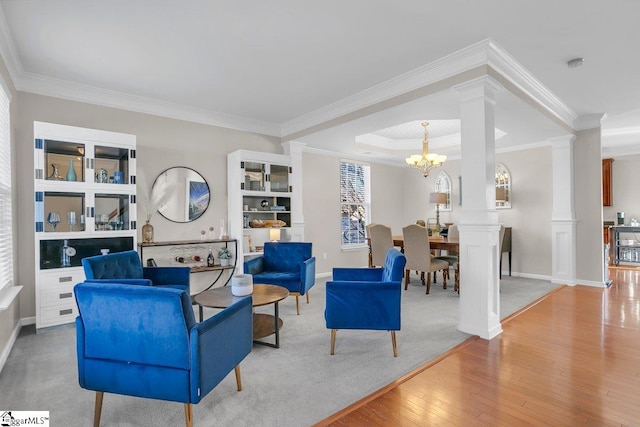 living room with an inviting chandelier, decorative columns, crown molding, light hardwood / wood-style floors, and a tray ceiling