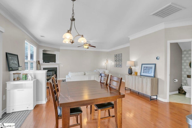 dining space with light wood-type flooring, ceiling fan with notable chandelier, and ornamental molding