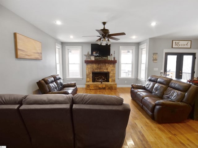 living room featuring ceiling fan, a stone fireplace, french doors, and light hardwood / wood-style flooring