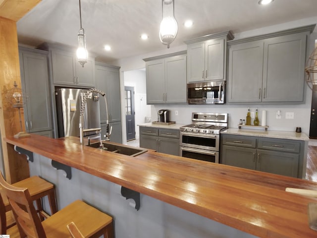 kitchen with stainless steel appliances, gray cabinetry, hanging light fixtures, and wooden counters