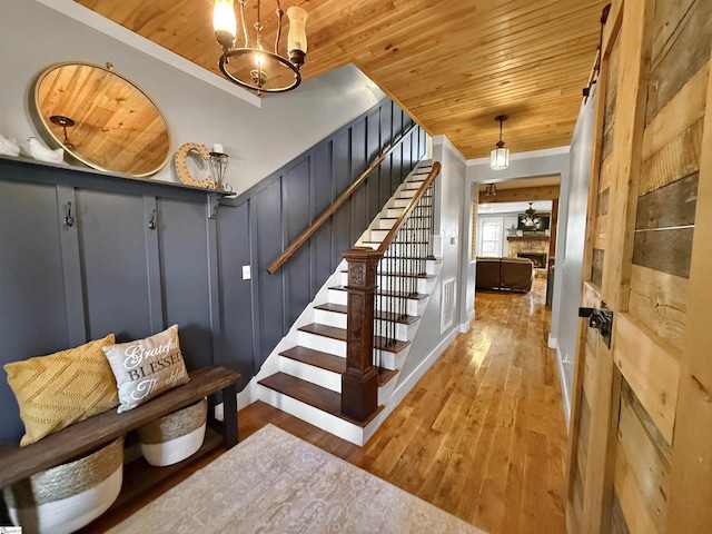 stairway with crown molding, a stone fireplace, wooden ceiling, and wood-type flooring