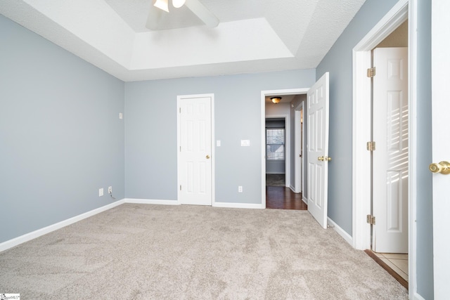 unfurnished bedroom with a textured ceiling, light colored carpet, a raised ceiling, and ceiling fan