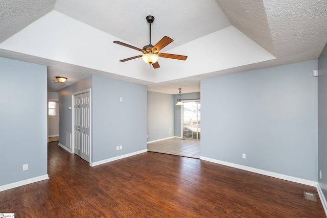 unfurnished room featuring ceiling fan, dark hardwood / wood-style flooring, a raised ceiling, and a textured ceiling