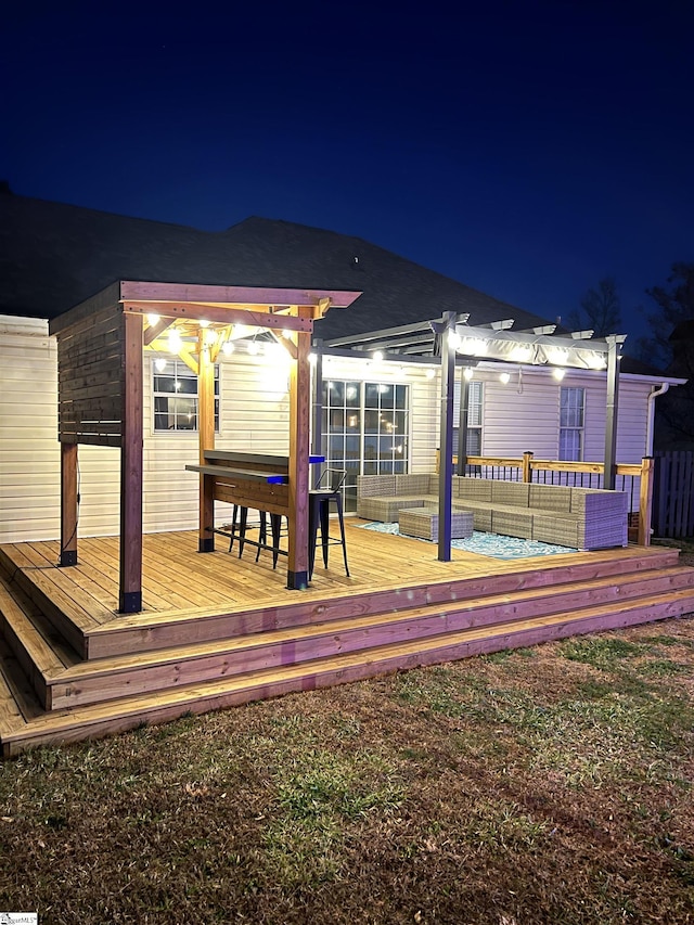 back house at night featuring an outdoor living space, a deck, and a pergola