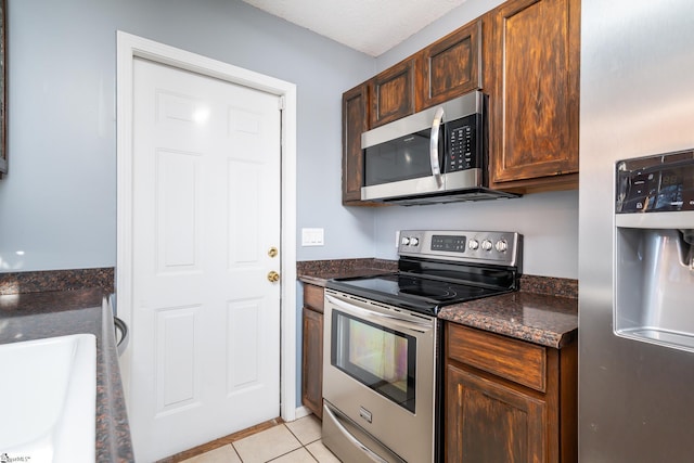 kitchen featuring dark stone countertops, sink, light tile patterned flooring, and appliances with stainless steel finishes