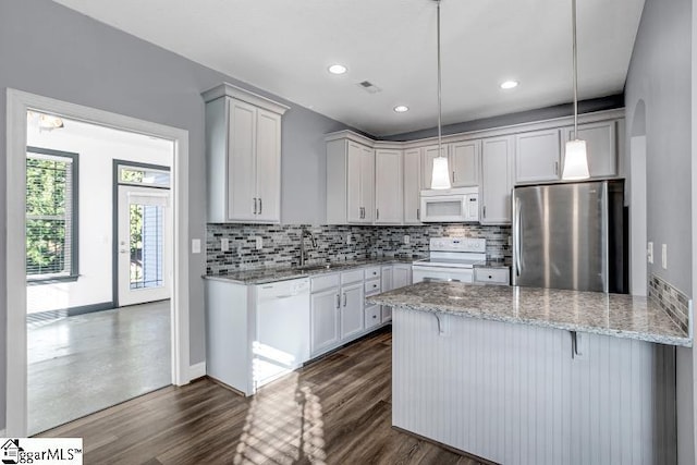 kitchen with white appliances, hanging light fixtures, light stone countertops, white cabinets, and sink