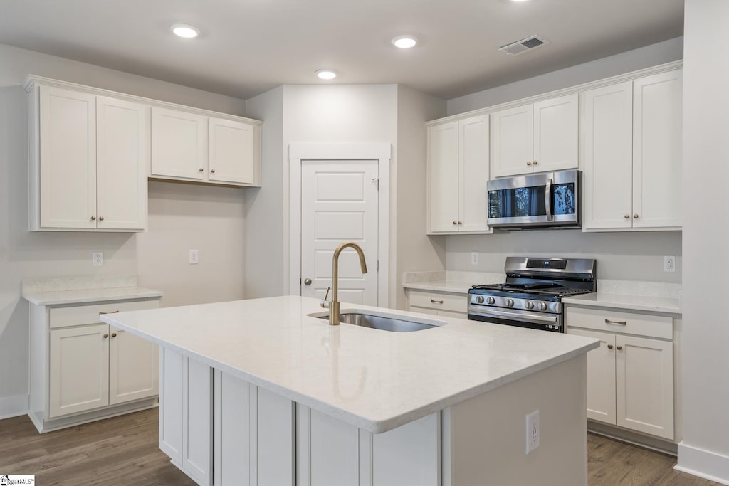 kitchen with appliances with stainless steel finishes, a kitchen island with sink, sink, light hardwood / wood-style floors, and white cabinetry