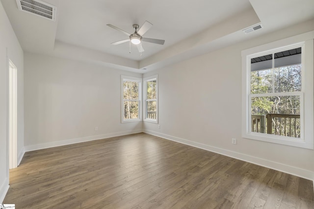 unfurnished room featuring a raised ceiling, ceiling fan, plenty of natural light, and dark hardwood / wood-style floors