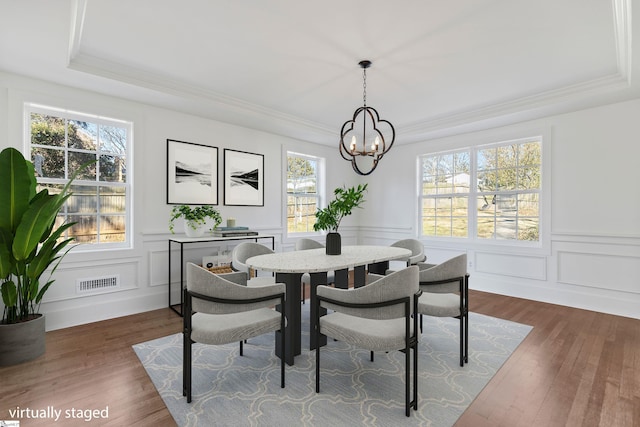 dining space featuring a chandelier, a raised ceiling, a wealth of natural light, and dark wood-type flooring