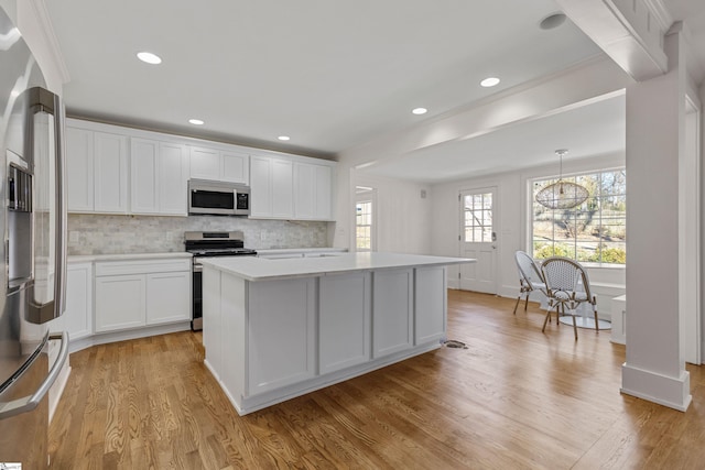 kitchen with pendant lighting, white cabinets, light wood-type flooring, a kitchen island, and stainless steel appliances