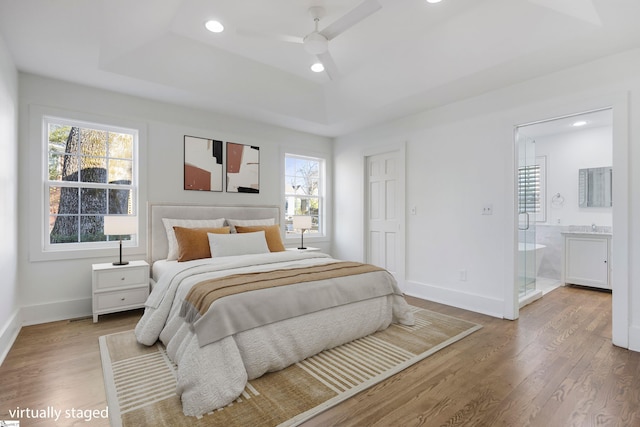 bedroom with ensuite bathroom, light hardwood / wood-style flooring, ceiling fan, and a tray ceiling