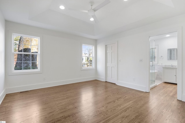 unfurnished bedroom with a raised ceiling, connected bathroom, and multiple windows