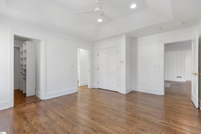 unfurnished bedroom with dark hardwood / wood-style floors, ceiling fan, and a raised ceiling