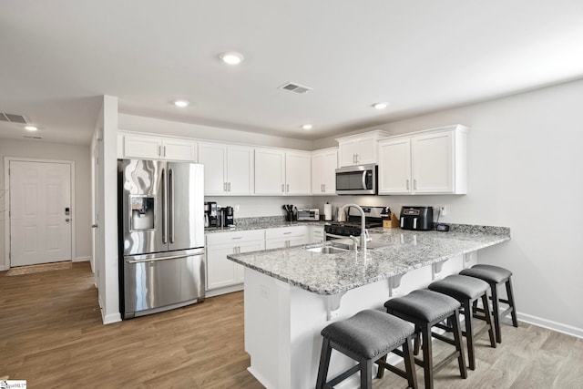 kitchen with kitchen peninsula, appliances with stainless steel finishes, white cabinetry, and sink