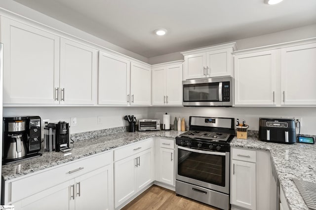 kitchen featuring light hardwood / wood-style floors, light stone countertops, white cabinetry, and appliances with stainless steel finishes