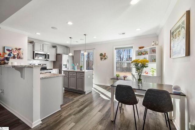 kitchen featuring gray cabinetry, light stone countertops, hanging light fixtures, a breakfast bar, and appliances with stainless steel finishes